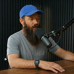 Bearded creator in a blue cap at a podcast mic